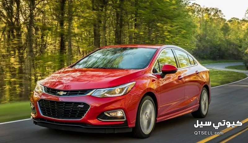 سيارة شيفروليه حمراء تسير على طريق تحيط به الأشجار